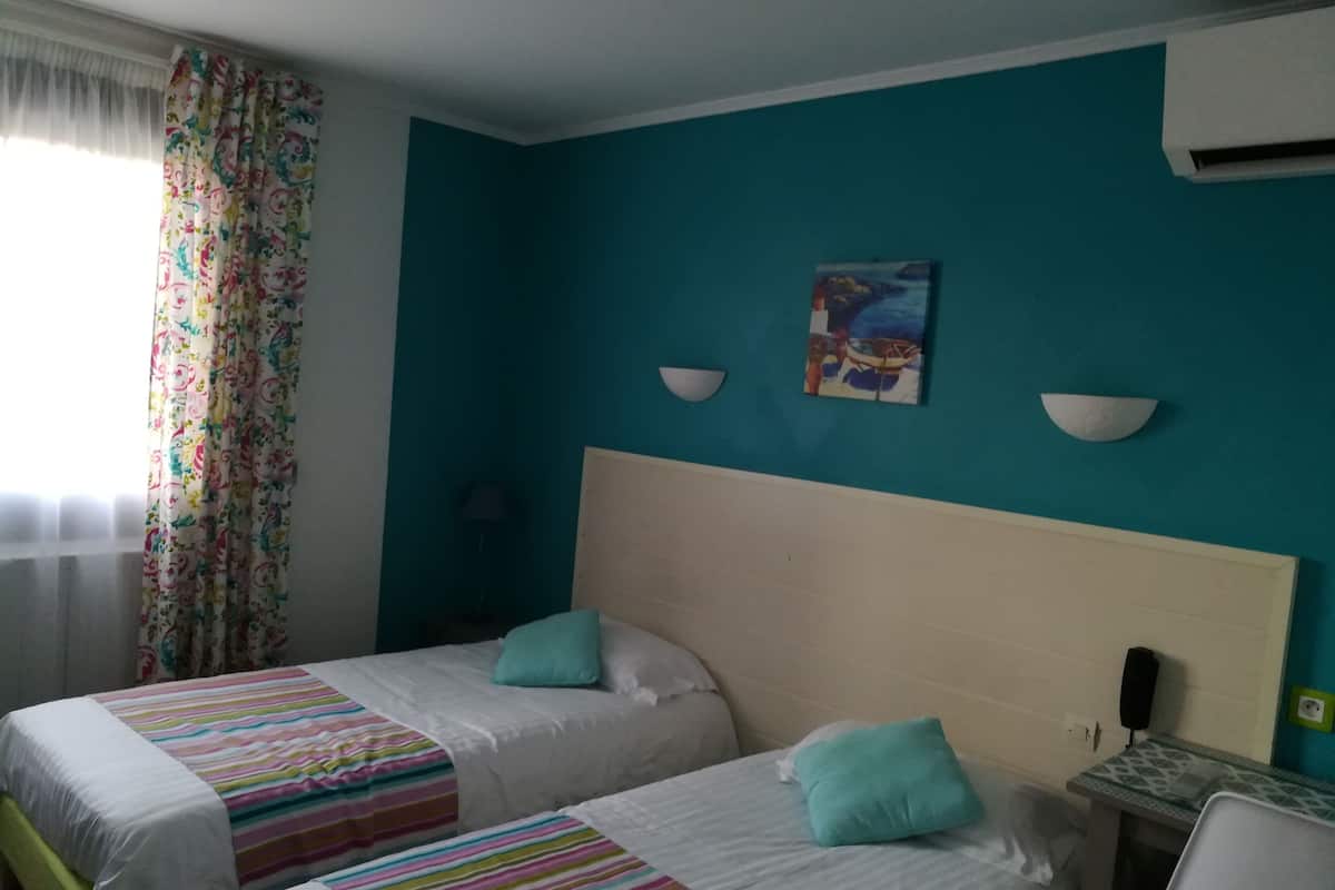 A hotel room with two beds, a desk, a chair, a painting, and a window with curtains.
