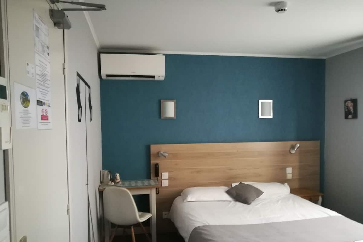 A hotel room with a bed, a desk, and an air conditioning unit.