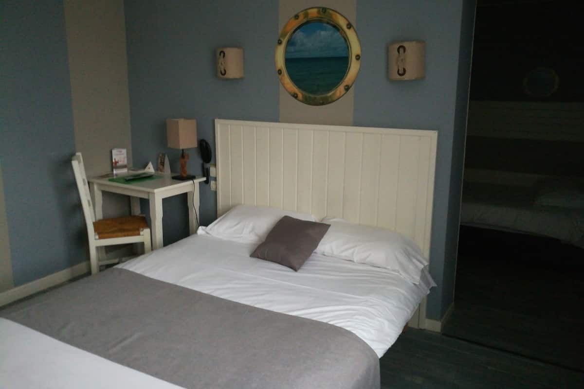 A hotel room with a bed, a desk, a chair, a lamp, and a wall-mounted mirror.
