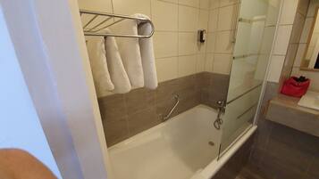 Et moderne badeværelse med badekar, brusekabine i glas og en rød taske på en hylde.