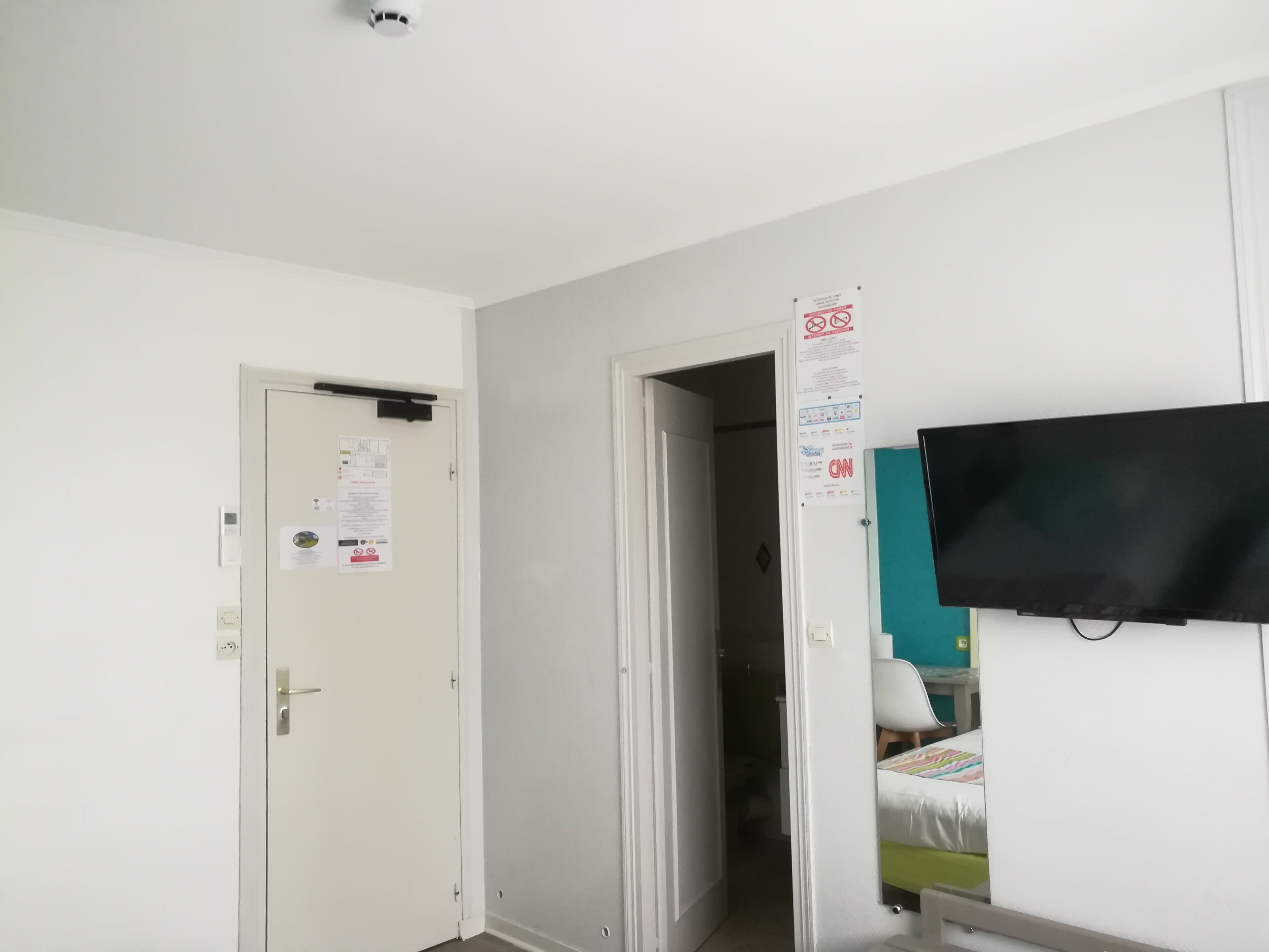 A room with a white door, a television mounted on the wall, and a door with a sign.