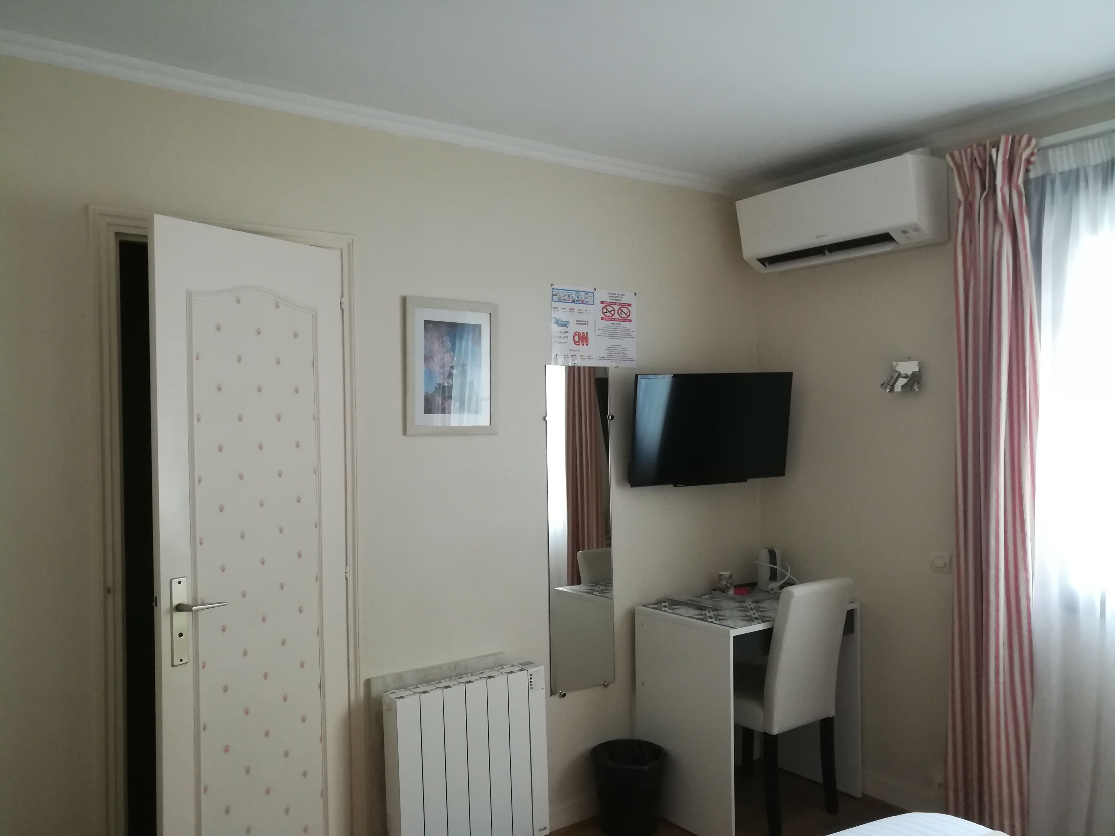 Ein Hotelzimmer mit einem Bett, einem Schreibtisch mit Stuhl, einem an der Wand befestigten Fernseher, einer Klimaanlage und einer Tür mit einem dekorativen Muster.