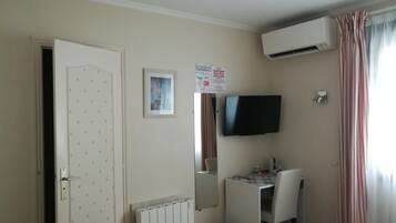 Ein Hotelzimmer mit einem Bett, einem Schreibtisch mit Stuhl, einem an der Wand befestigten Fernseher, einer Klimaanlage und einer Tür mit einem dekorativen Muster.