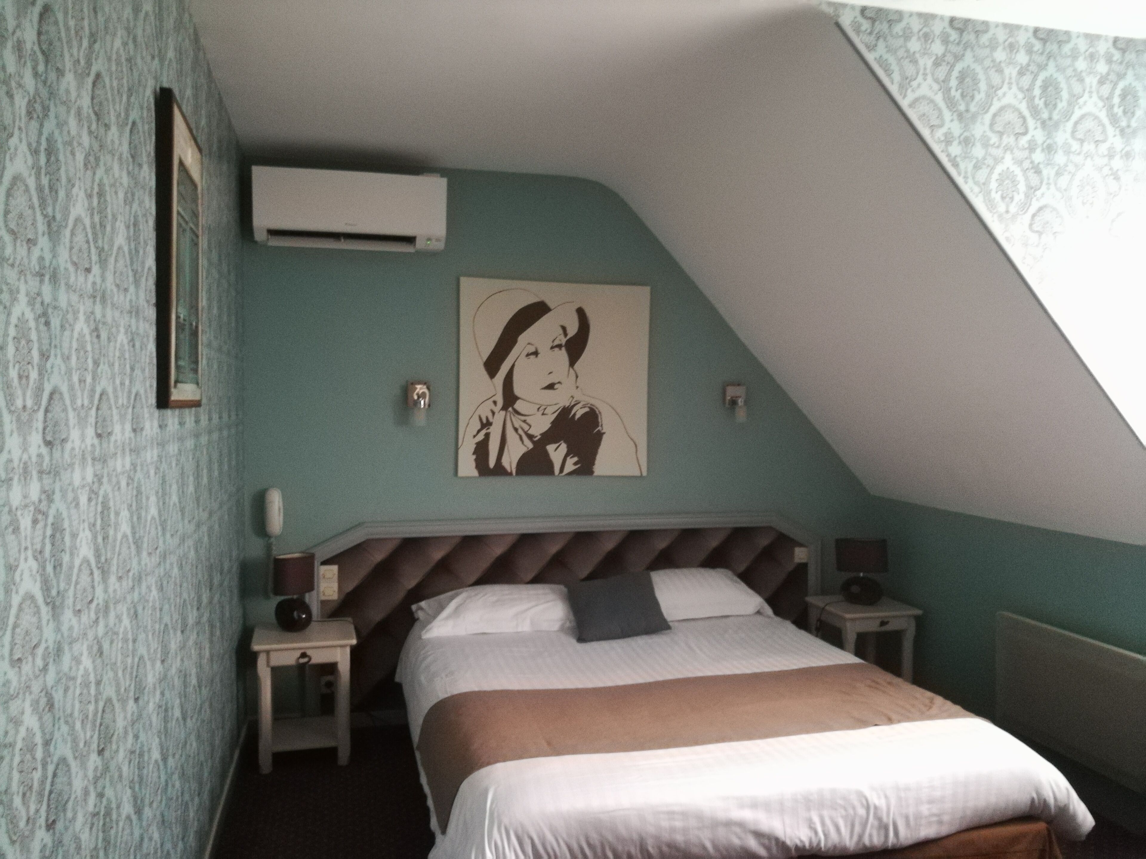 A bedroom with a bed, a nightstand, a wall-mounted air conditioner, and a painting.