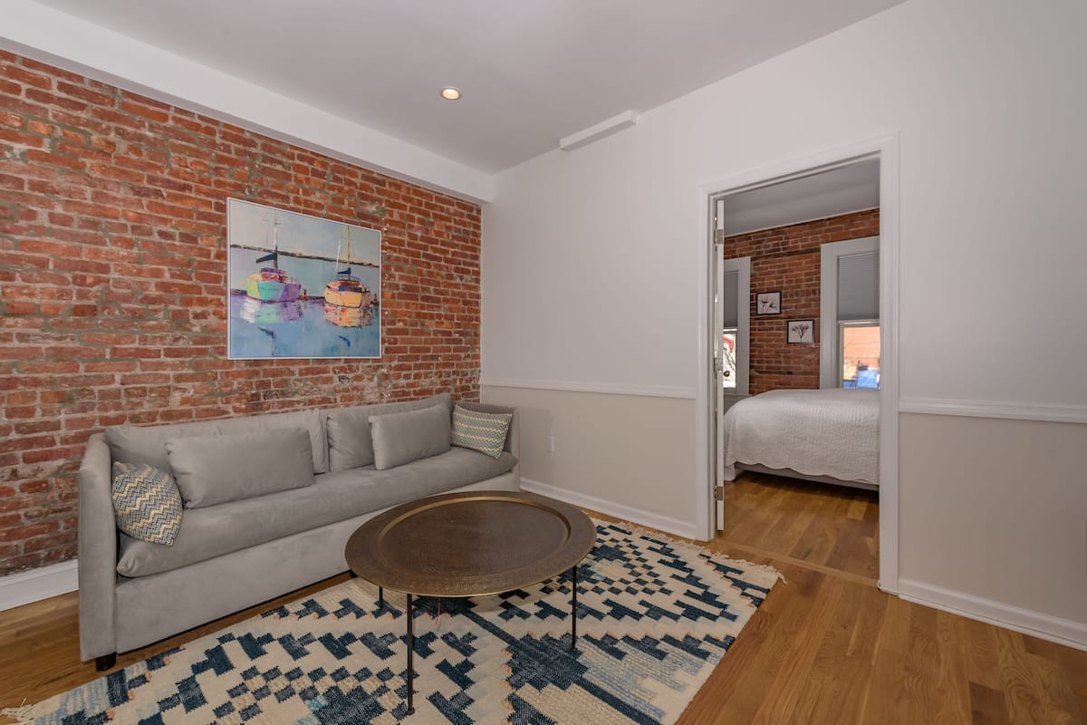 A living room with a brick wall, a gray sofa, a round coffee table, and a patterned rug.