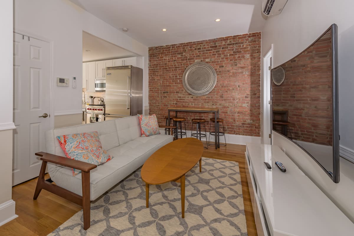 A modern living room with a white sofa, a wooden coffee table, and a brick accent wall.
