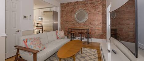 A modern living room with a white sofa, a wooden coffee table, and a brick accent wall.