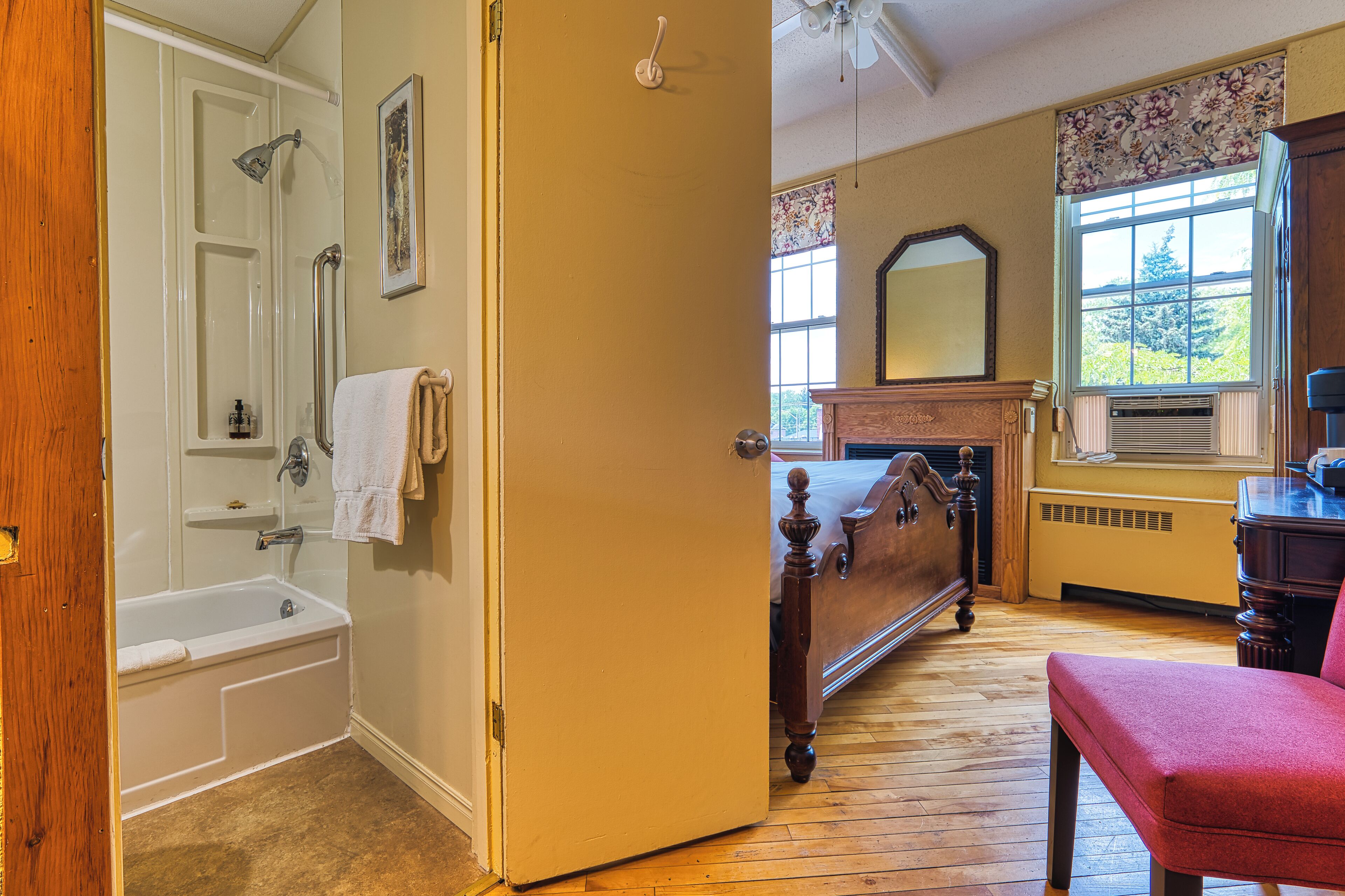 A bathroom with a bathtub, a wooden bench, a mirror, and a window with floral curtains.