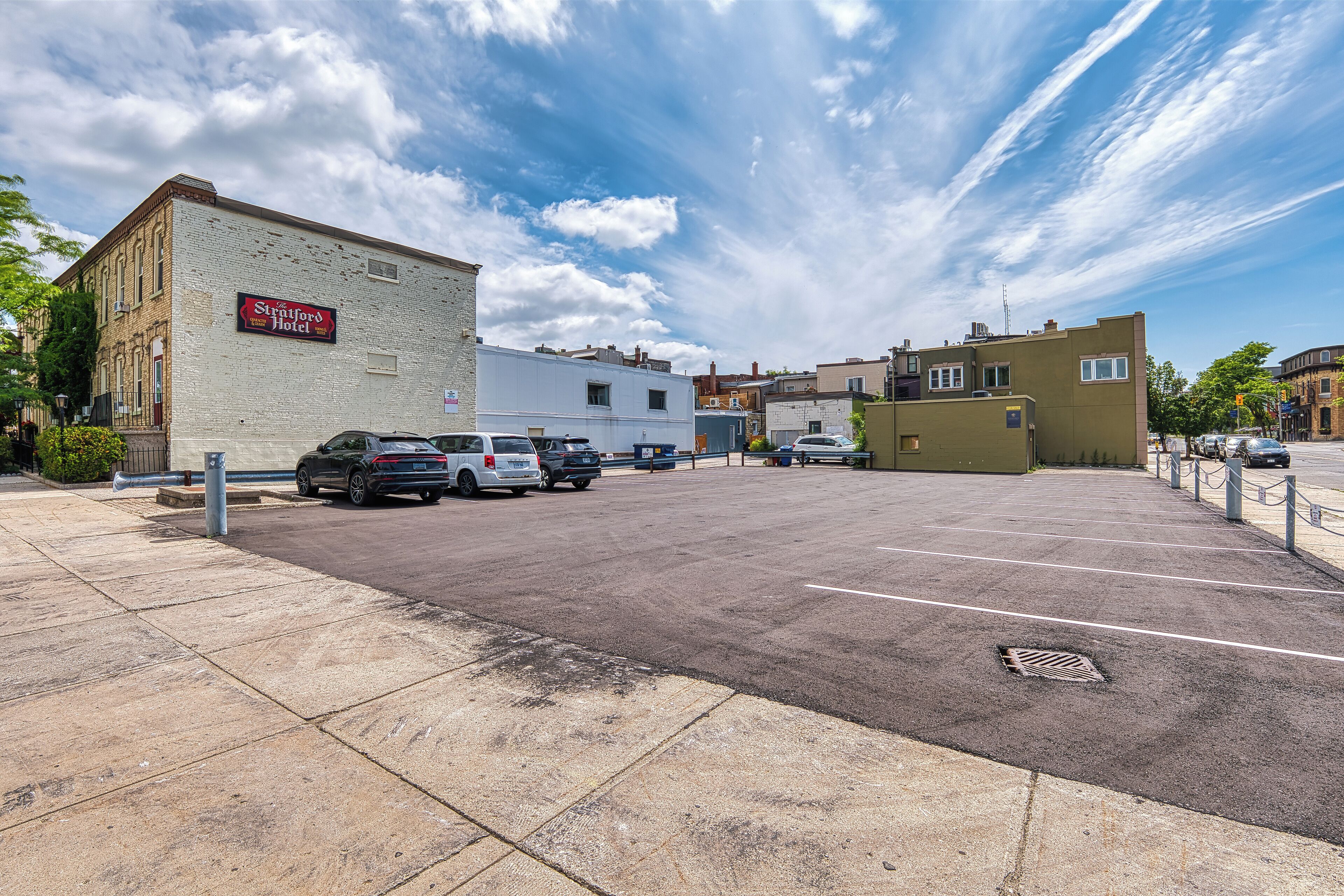 A parking lot with several cars, a building with a sign reading "Stratford Hotel," and a clear sky with clouds.