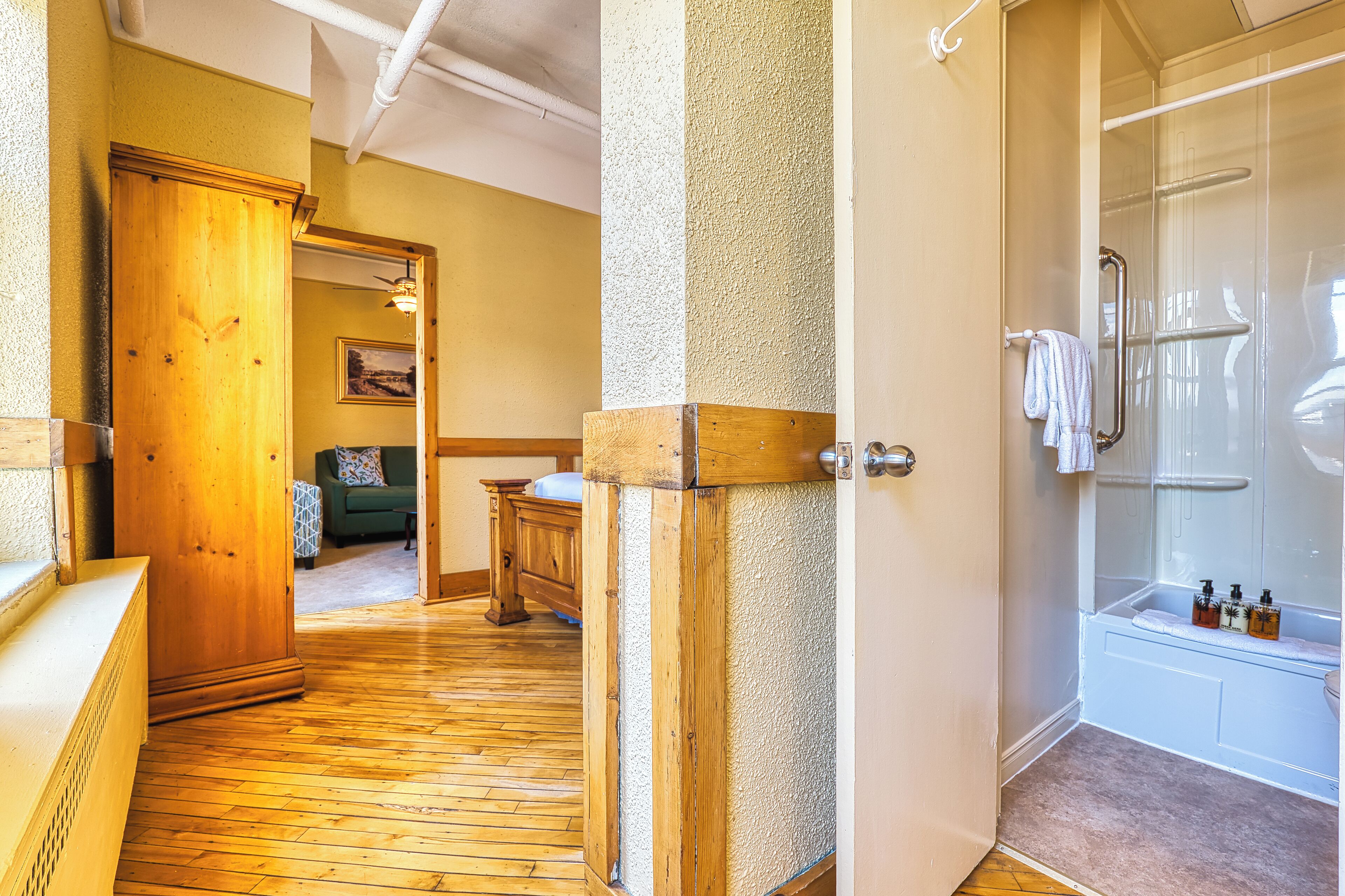 A wooden-floored hallway leading to a bathroom with a glass shower enclosure and a bathtub.
