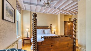 Una cama con dosel de madera y cabecera, una mesita de noche con lámpara, un radiador y un cuadro en la pared.