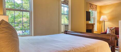 A hotel room with a large bed, a chair, a lamp, and a window with a view of trees.