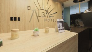 Bancada de recepção de hotel com acabamento em madeira, um logotipo em formato de sol e um balcão de atendimento.