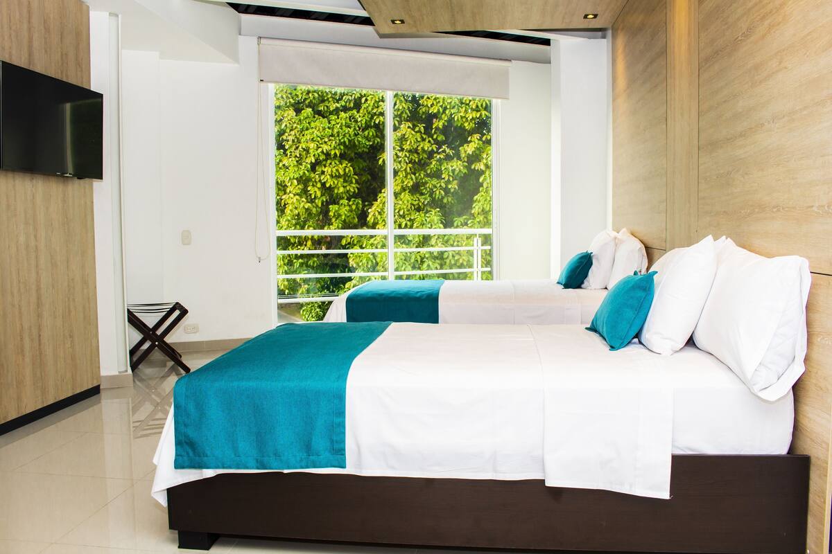 Ein modernes Hotelzimmer mit zwei Betten, einem Fernseher und einem Balkon mit Blick auf Bäume.