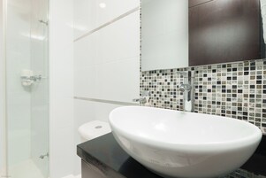 Un baño con lavamanos blanco, cabina de ducha de cristal y salpicadero de azulejos.