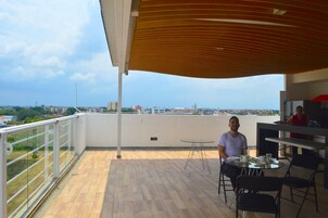 Un balcón con suelo de madera, una mesa con sillas y vista panorámica de la ciudad.
