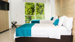 Quarto de hotel moderno com duas camas, televisão e varanda com vista para vegetação.