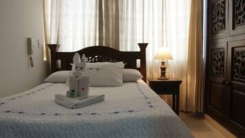 A hotel room with a bed, a nightstand with a lamp, a towel animal, and a bottle of lotion.