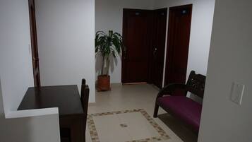 Una habitación con una mesa de comedor, un sofá morado, una planta en maceta y una puerta con manija.