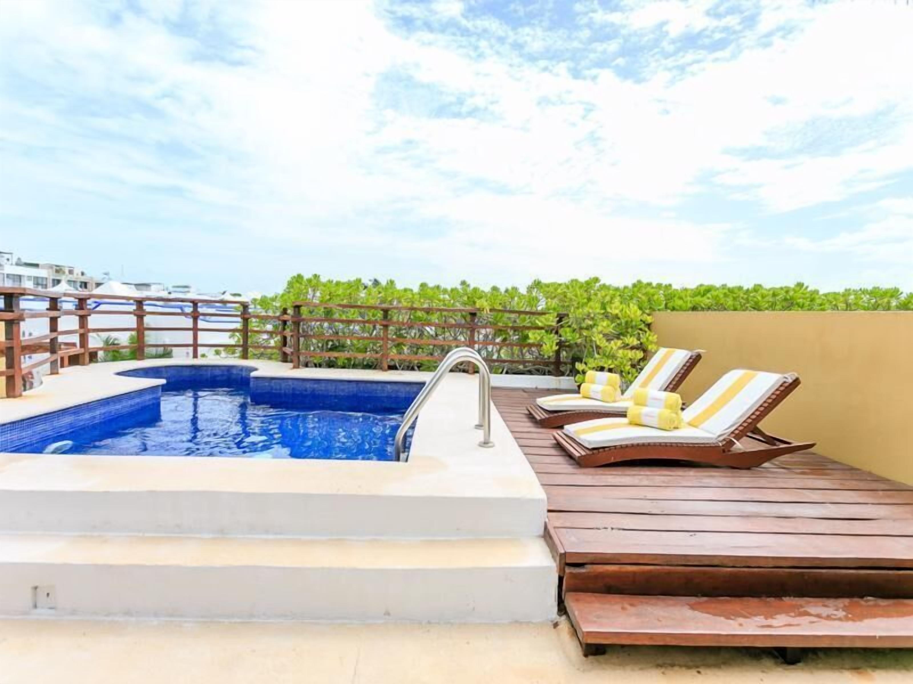 A rooftop pool with a wooden deck, lounge chairs, and a metal faucet.