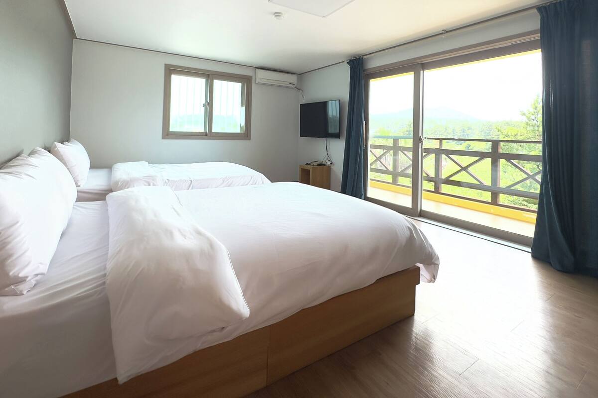 A bedroom with a large bed, a TV, and a balcony with a view.