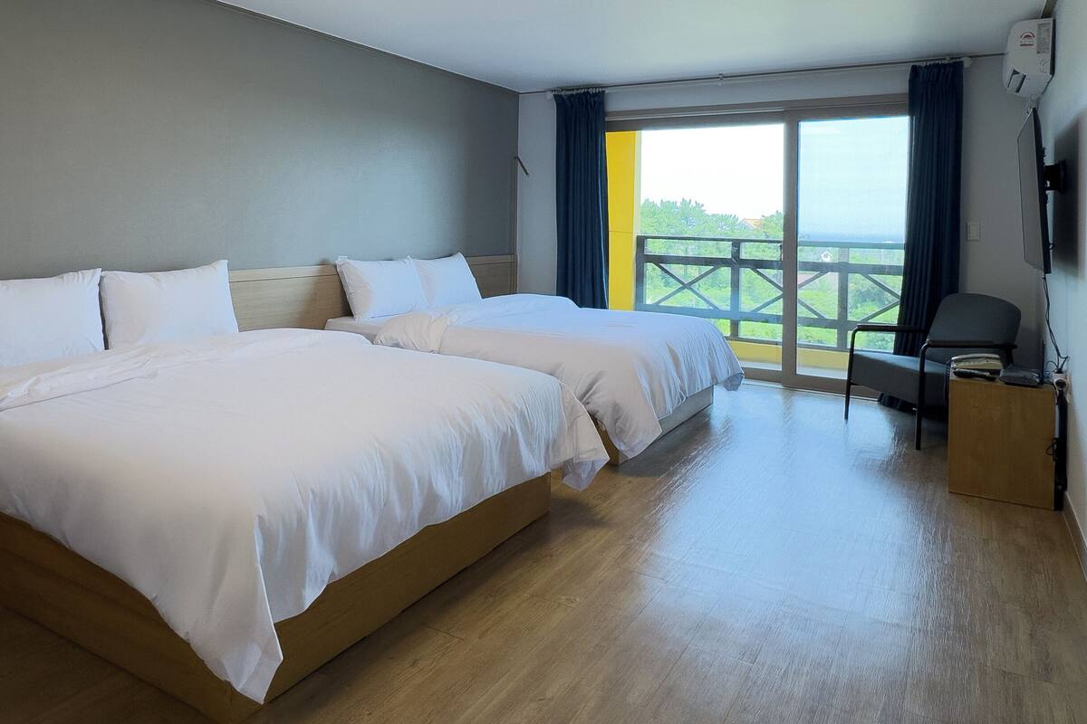 A hotel room with two beds, a wooden floor, a balcony with a view, and a chair.