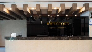 Rezeption des WHINSTONE HOTEL & RESORT mit Marmorzauber, Holzbalken und einer Uhr an der Wand.