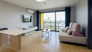Ein modernes Wohnzimmer mit einer Couch, einem Couchtisch, einem an der Wand befestigten Fernseher und einem Balkon mit Geländer.