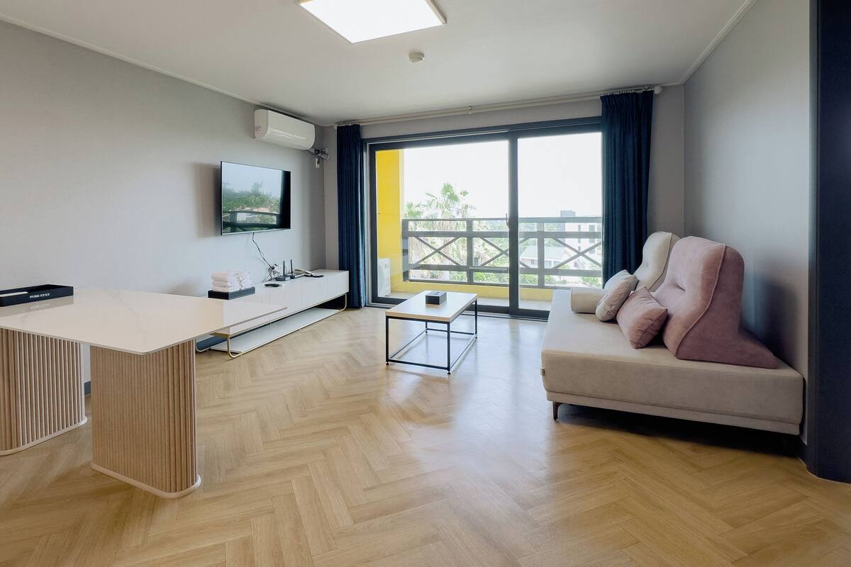 A modern living room with a sofa, a coffee table, a TV mounted on the wall, and a balcony with a railing.