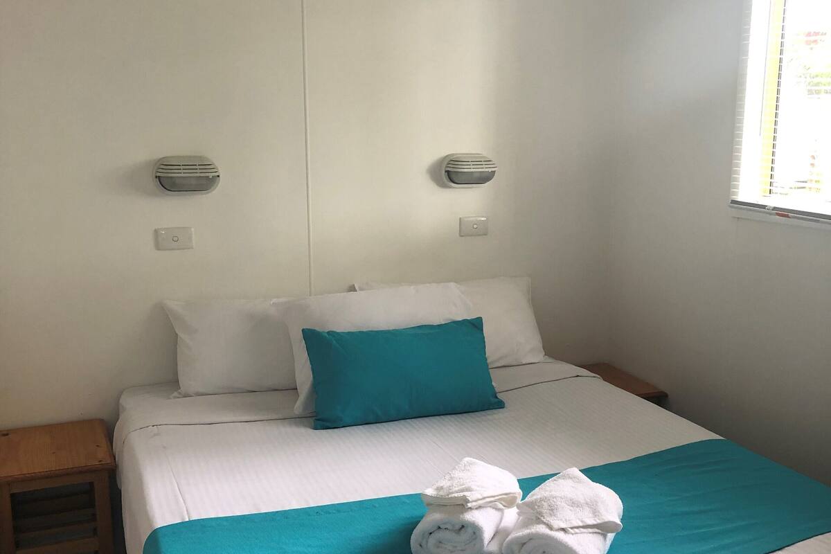 A neatly made bed with a teal bedspread and white bedding, a teal pillow, and a sign above reading "DREAM BEACH SUN".
