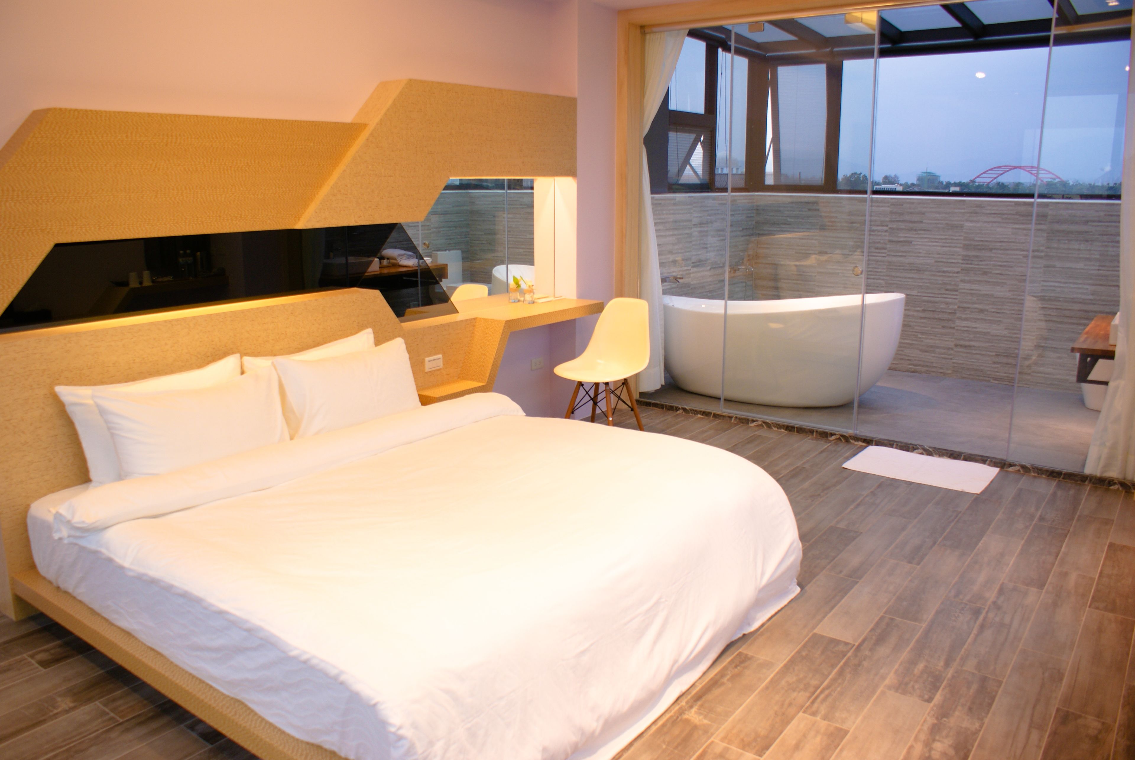 Quarto moderno com cama grande, escrivaninha e varanda envidraçada com vista.