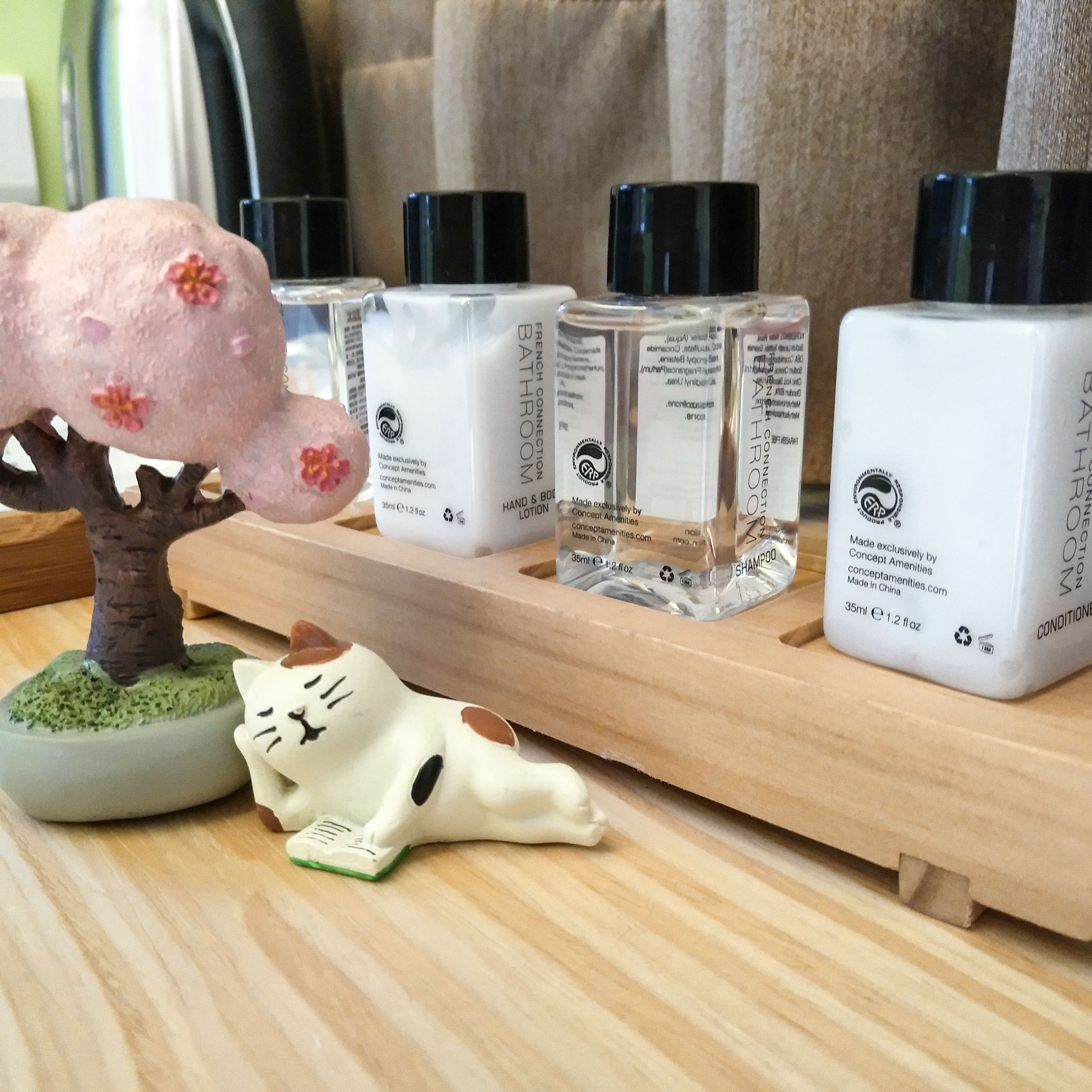 A wooden tray with various toiletries including a pig figurine, a cat figurine, and several bottles of hand and body care products.