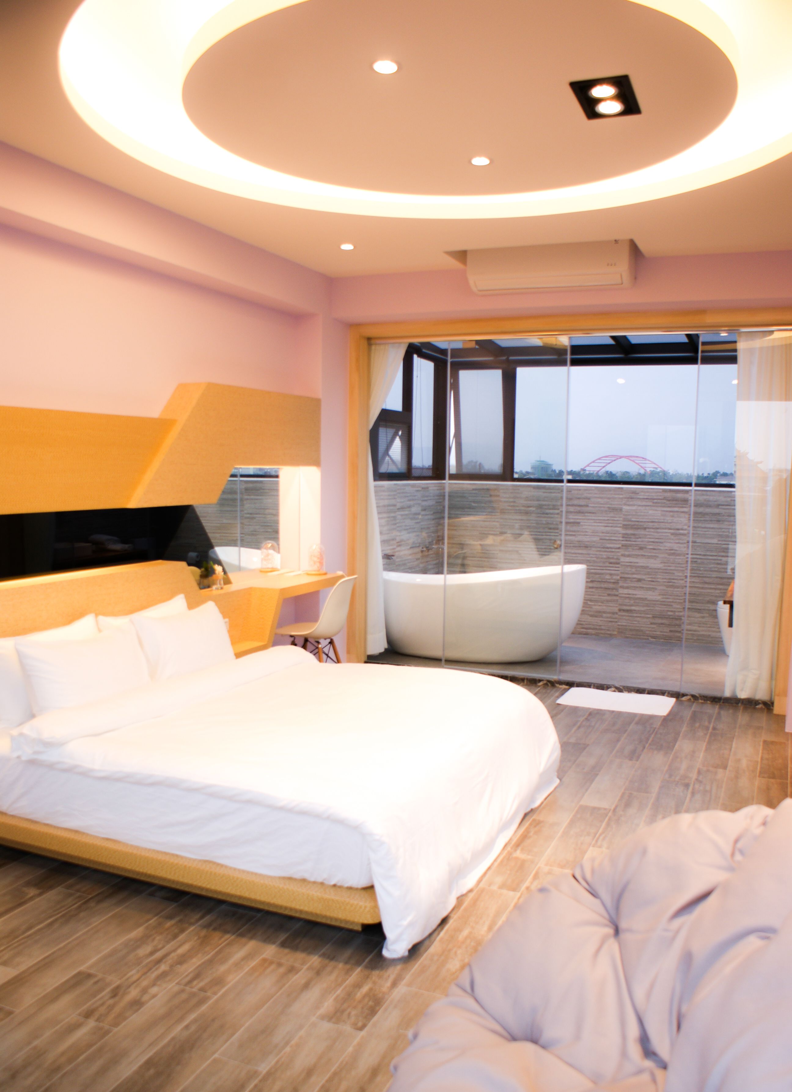 A modern bedroom with a large bed, a seating area, and a view of a bridge through a glass door.