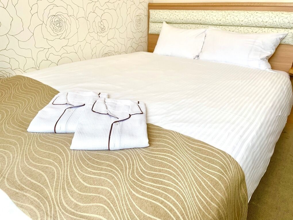 Una cama bien hecha con una colcha estampada y almohadas, junto con un par de pantalones de dormir blancos doblados sobre la cama.