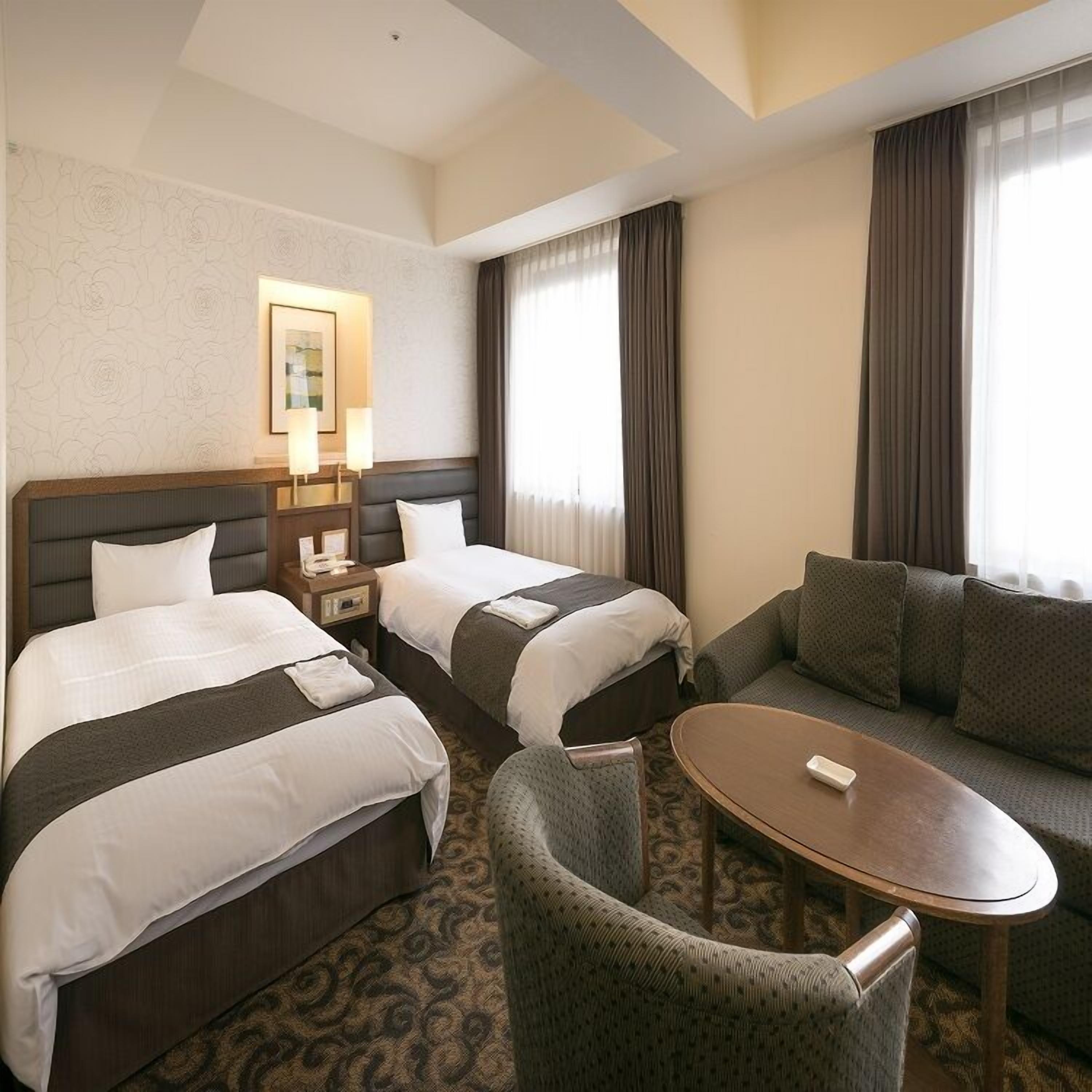 Habitación de hotel con dos camas, un sofá, una mesita y una mesilla de noche.