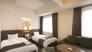 A hotel room with two beds, a sofa, a small table, and a nightstand with a lamp.