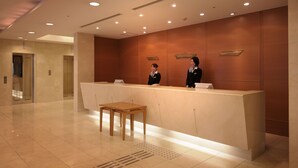 A reception area with a reception desk, two receptionists, a wooden table, and a tiled floor.