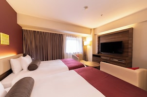 A hotel room with two beds, a TV, a desk, and a chair.