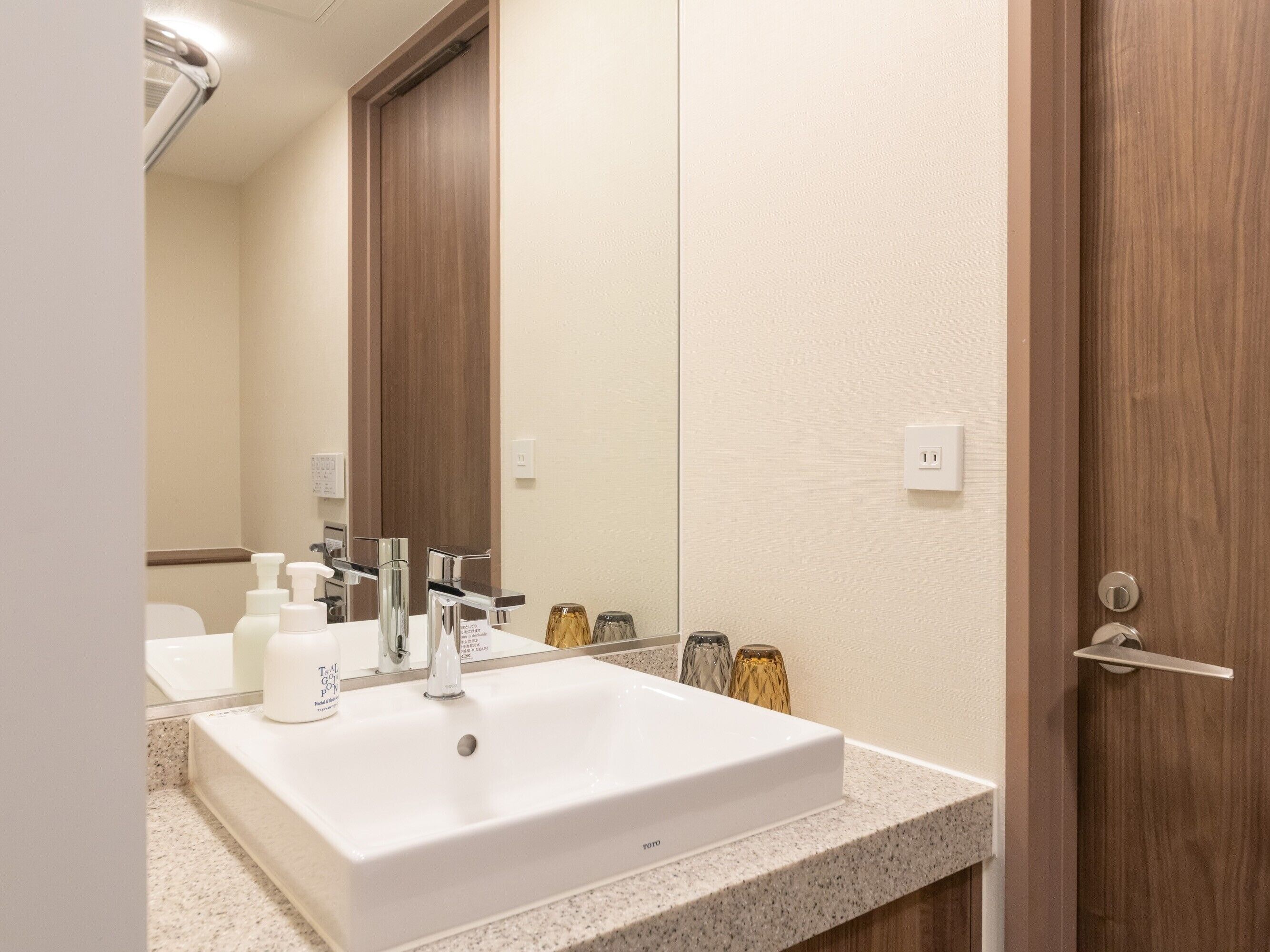 A hotel bathroom with a white sink, a mirror, and a wooden door.