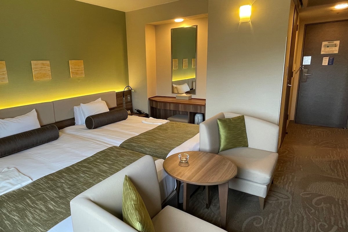 A hotel room with a large bed, two bedside tables, a small round table, and a sofa.