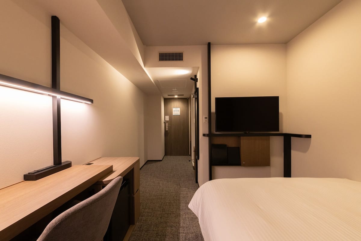 A hotel room with a bed, desk, chair, and a television on a stand.