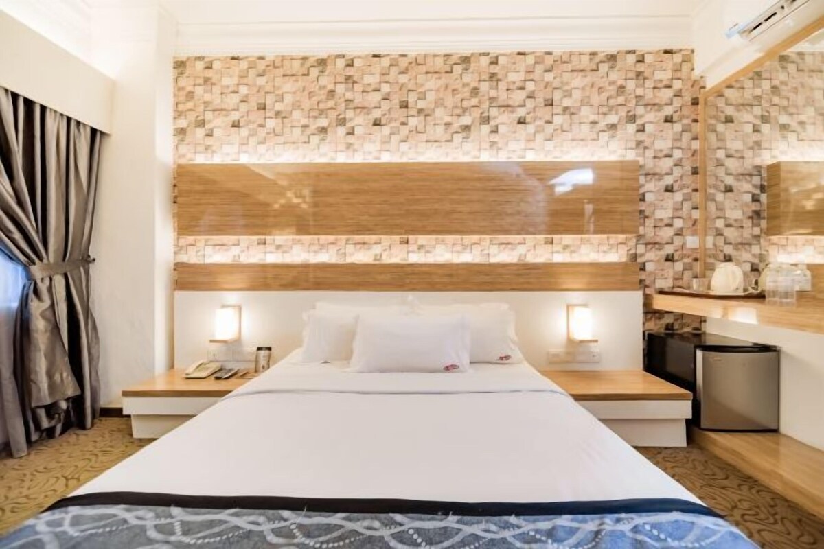 A hotel room with a large bed, bedside tables, a mirror, and a small kitchenette.