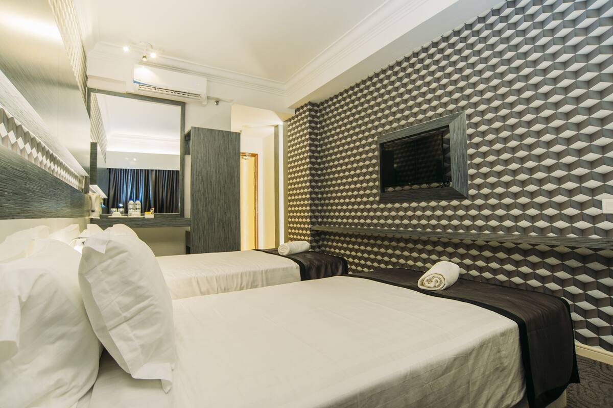 A hotel room with two beds, a large mirror, a TV, and a patterned wall.