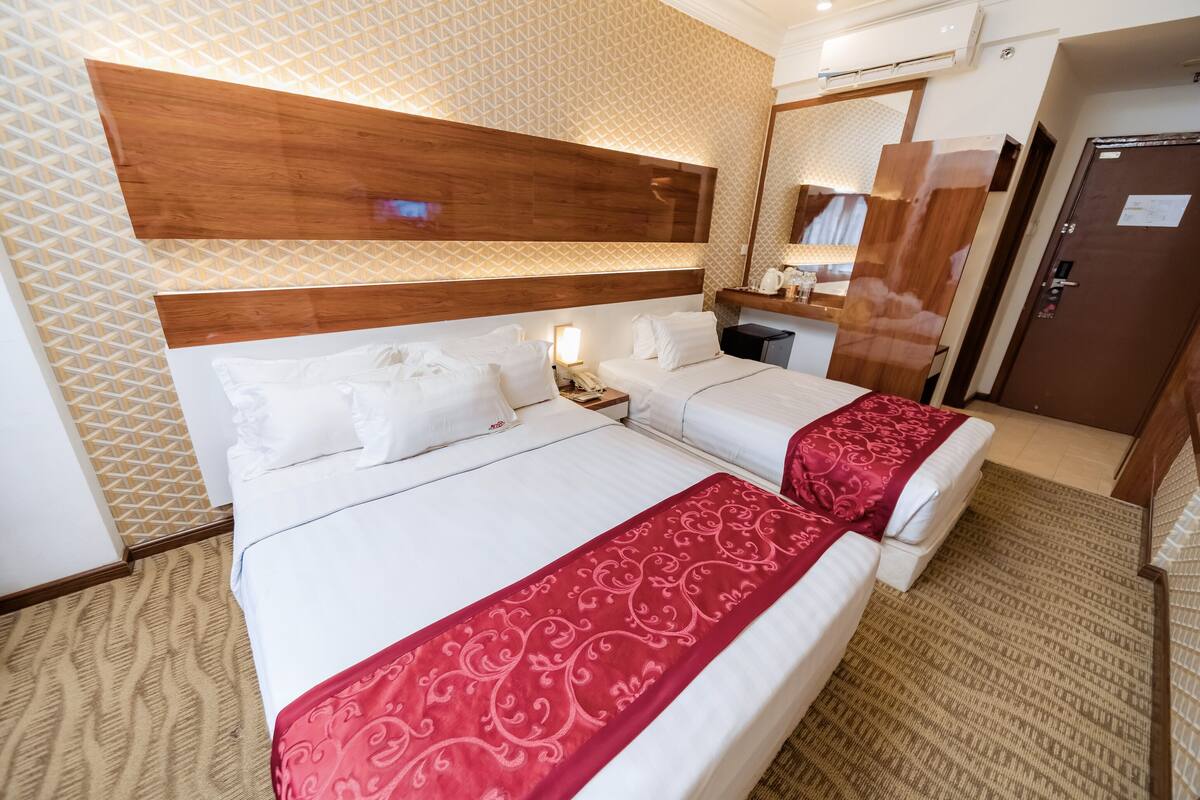 A hotel room with two beds, a wooden headboard, a minibar, and a bathroom door.