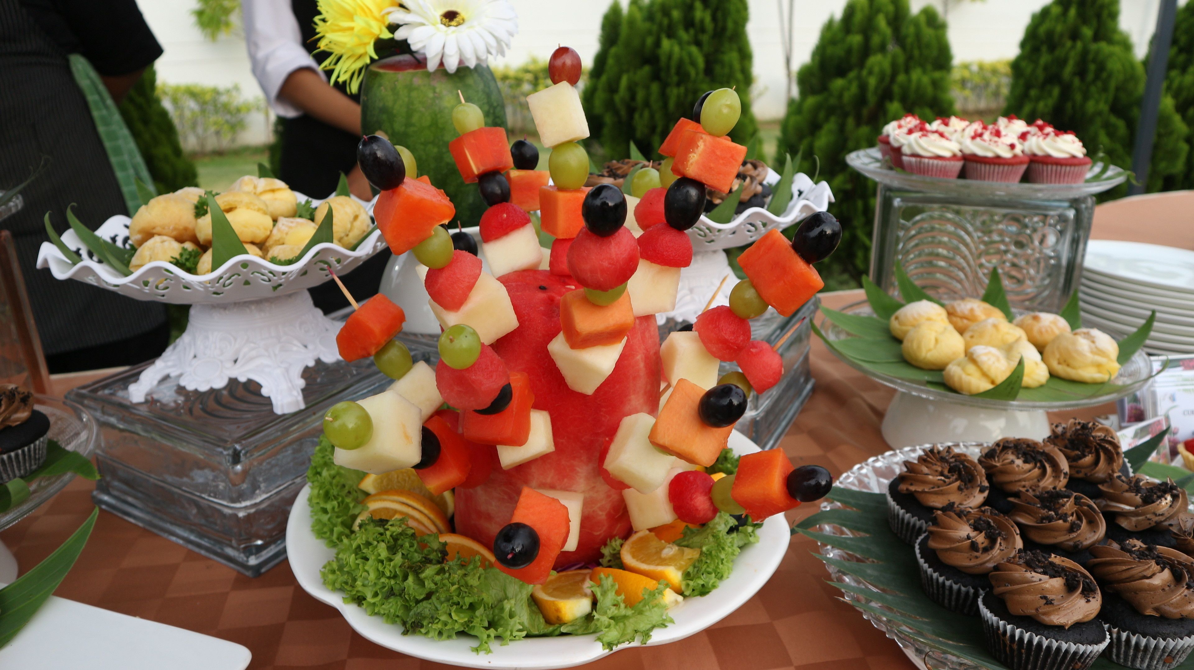 A buffet table with various food items including fruit skewers, cupcakes, and pastries.
