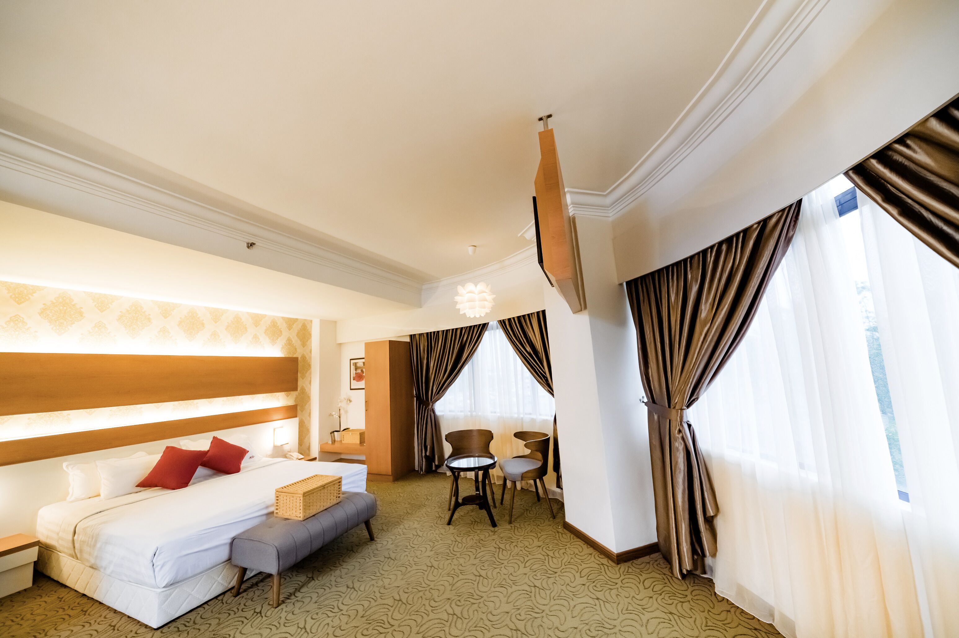 Una habitación de hotel con cama, mesitas de noche, escritorio, silla y ventana con cortinas.