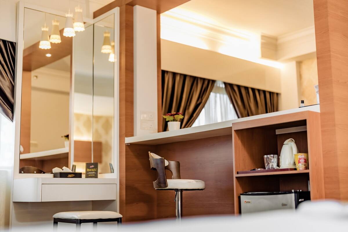 A modern hotel room with a large mirror, a vanity with a sink, a chair, and a shelf with toiletries.