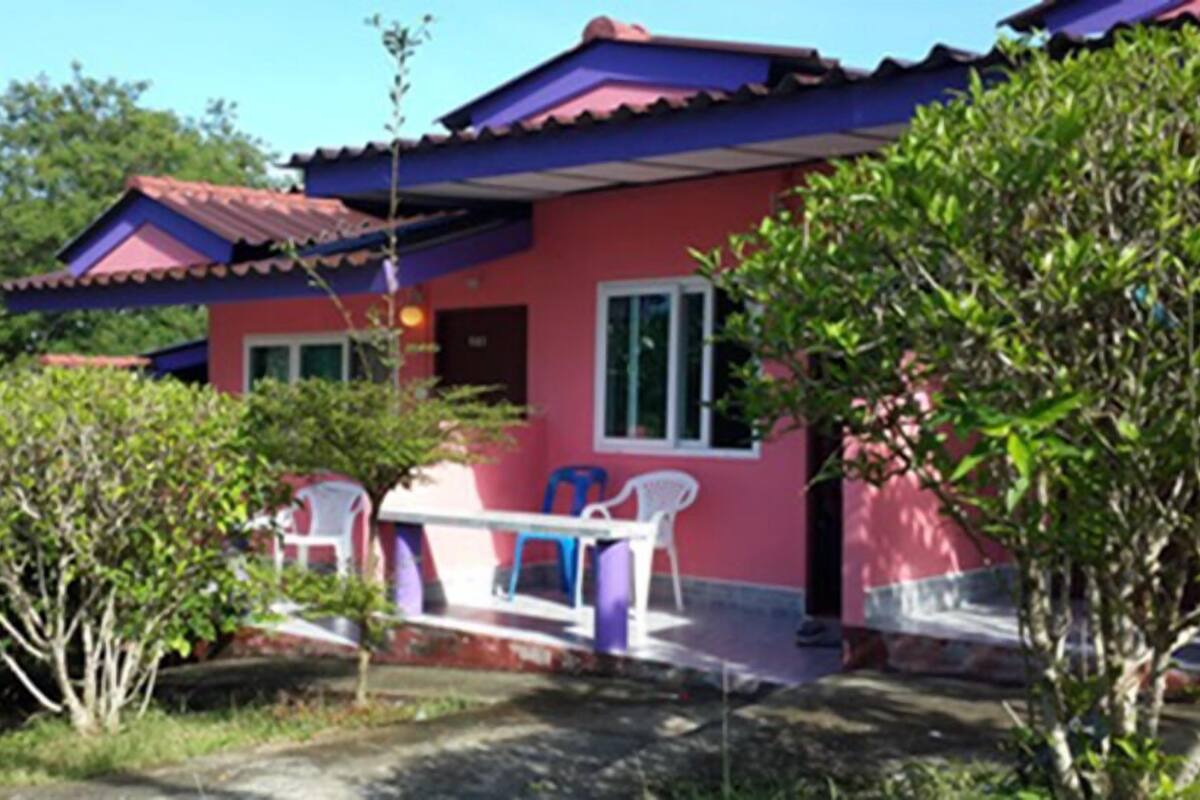 A pink house with a red roof, a small porch, and two white plastic chairs.