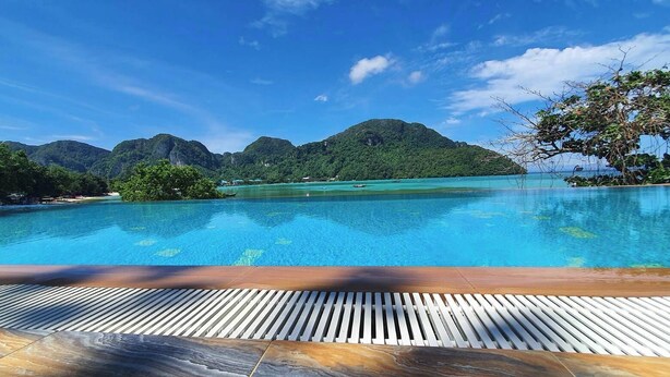 A swimming pool with a wooden deck in the foreground and a view of a mountainous landscape in the background.