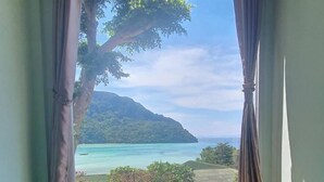 A room with a large window offering a view of a beach, a tree, and a distant island.